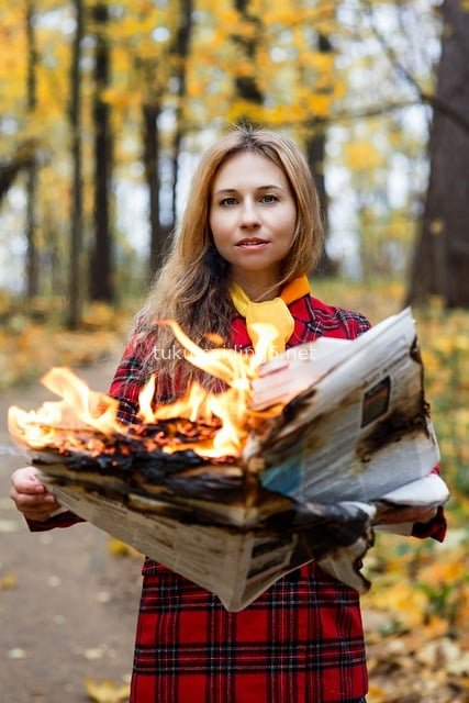 Woman in Plaid Coat Holding Burning Newspaper in Autumn Park
