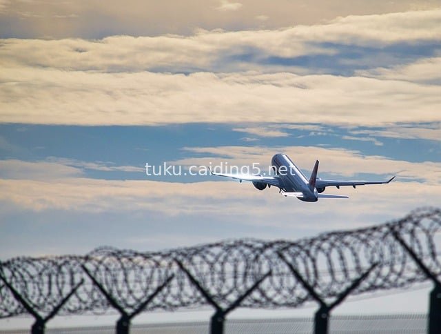Plane Taking Off Above Airport Barbed Wire Fence and Cloudy Sky