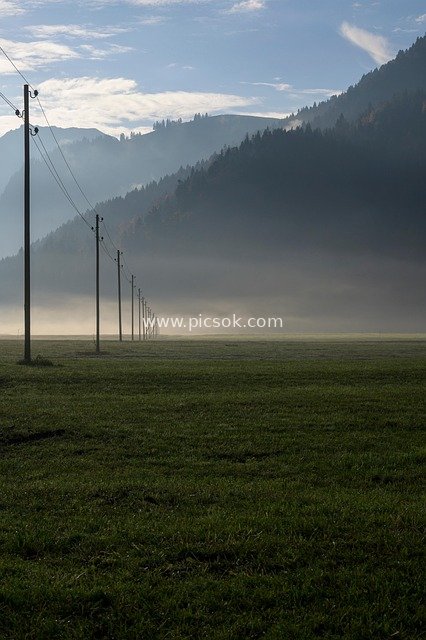 Alpine Mountains Veiled in Morning Mist: Transmission Lines Stretching Across the Grassland