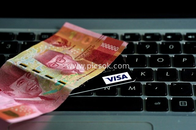 Visa Card and Indonesian Rupiah Cash on Laptop Keyboard