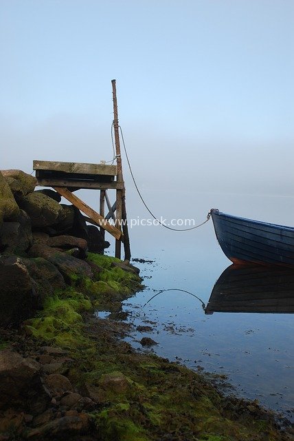 Boat Docked at Wooden Pier in Morning Fog: Quiet Coastal Scene with Rocks and Moss