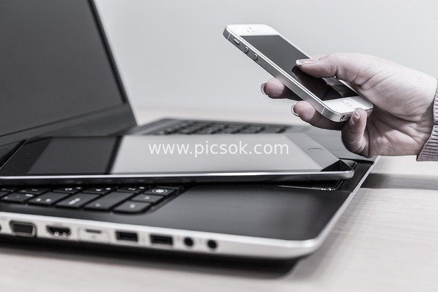 Tech Device Scene: Hand Holding Smartphone with Laptop & Tablet in Background