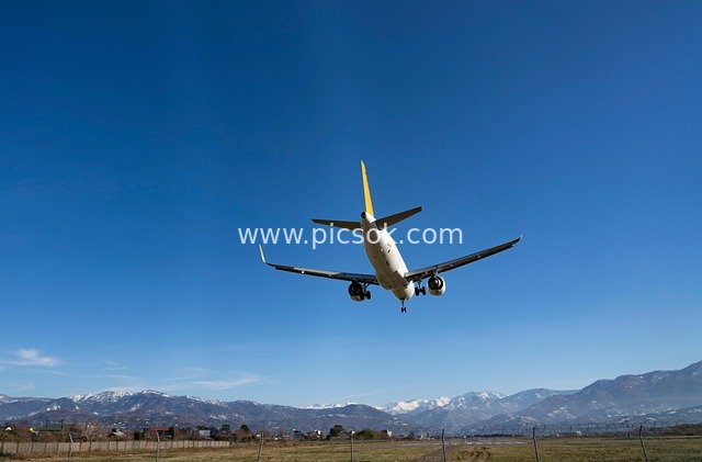 Commercial Airliner Landing Against Clear Blue Sky and Snow-Capped Mountains