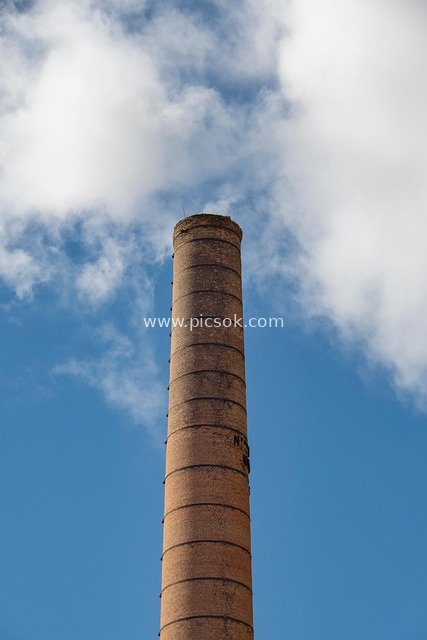 Abandoned Red Brick Chimney: Industrial Relic Under Blue Sky and White Clouds