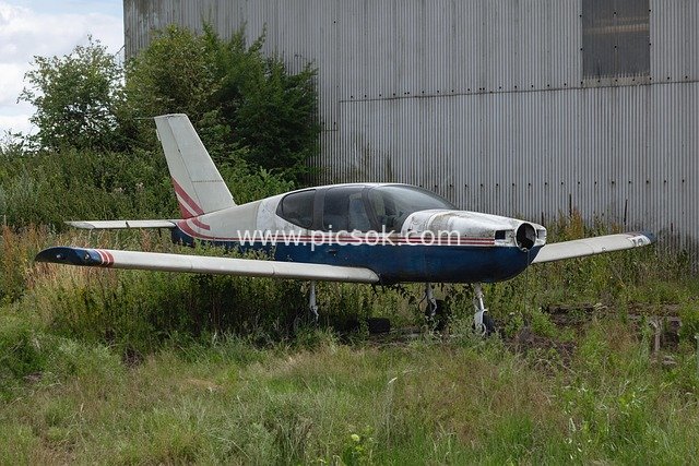 Abandoned Small Plane in the Grass and Old Aviation Equipment by the Hangar