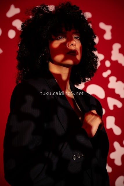Fashion Portrait of a Curly-Haired Woman in Black Suit Against Red Artistic Background