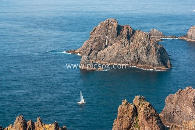 Tranquil Scene of a Sailboat Navigating Rocky Coastlines in the Blue Ocean