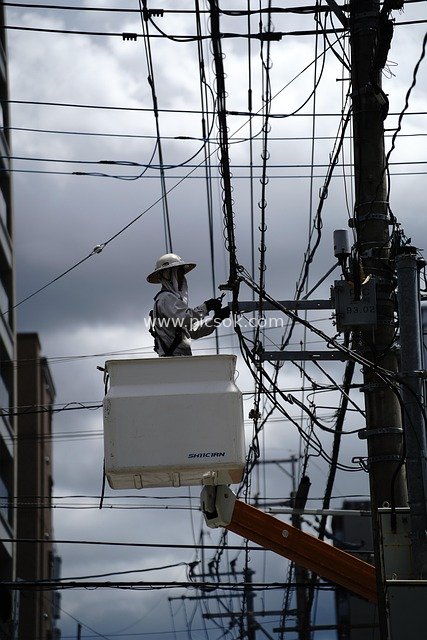Urban High-Altitude Electrician Repairing Cluttered Wires: Power Construction Under Cloudy Skies