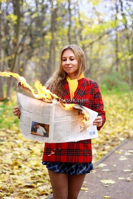 Beautiful Young Woman Holding Burning Newspaper in Autumn Park Showcases Fashionable Outfit and Charm