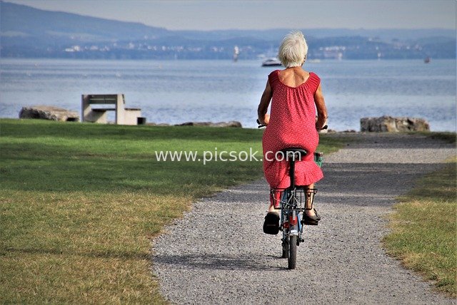 Elderly Woman in Red Dress Enjoying a Leisurely Bike Ride by Lake Bodensee