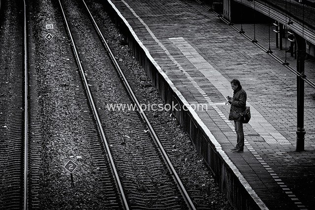 Black and White Street Photography: A Man Contemplating by Railway Tracks at a Train Station Platform