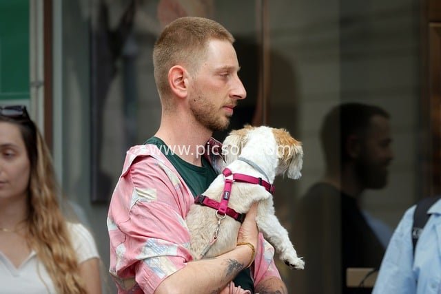 Urban Street: A Daily Moment of a Young Man Queuing with His Pet Dog Cradled in Arms