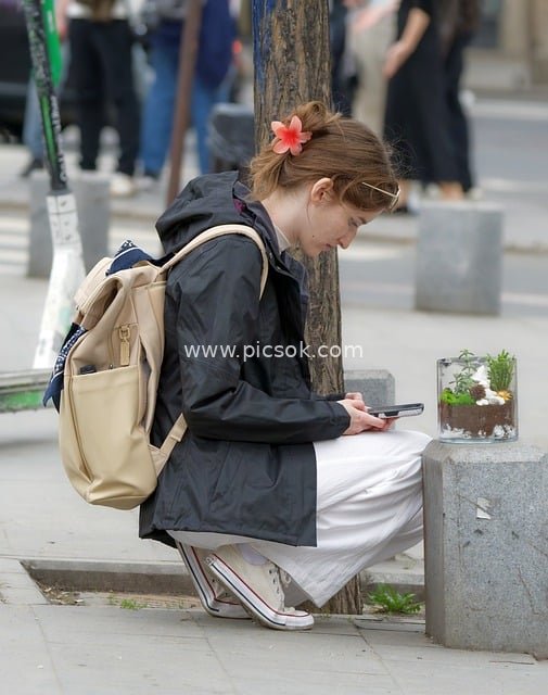 Casual Urban Girl Looking at Phone on City Street, Backpack Outfit in Daily Scene