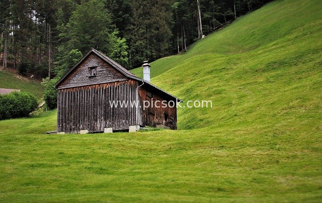 Old Weathered Wooden Chalet in Swiss Mountains with Lush Green Meadow Pastoral Landscape
