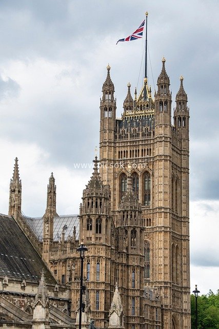 Tower of the Palace of Westminster in London with UK Flag and Cloudy Sky