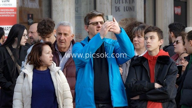 Crowd Waiting on Urban Street, Man Capturing Life with Smartphone