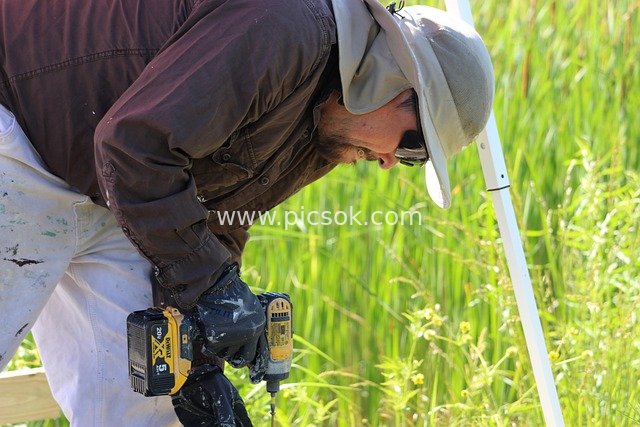 Real Shot of Outdoor Construction Worker Operating Cordless Drill at Work Site