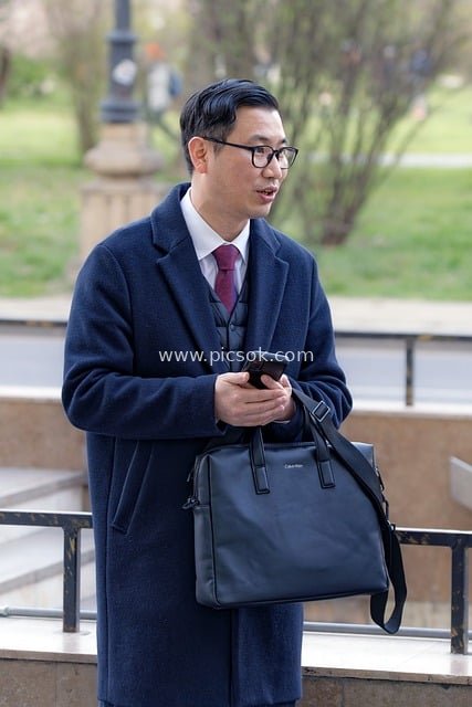 Asian Businessman Using Smartphone While Holding Bag in Outdoor Daily Scene