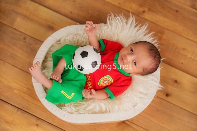 Heartwarming Newborn Photography: Baby in Football Kit Lying in Plush Basket