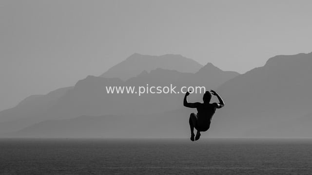 Black and White Silhouette: Man Leaping Over the Sea – A Dynamic Adventure Sports Moment