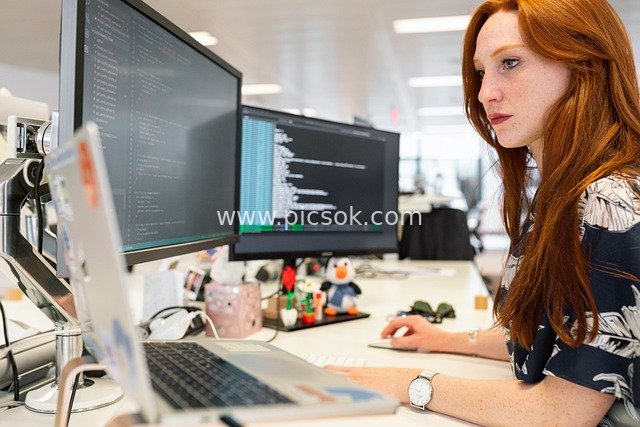 Scene of a Focused Red-haired Female Professional Working with Dual Monitors