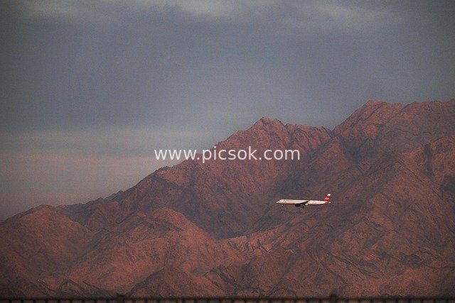 Airliner Flying Over Red-Brown Desert Mountains