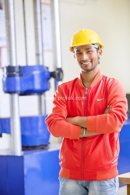 Engineer with Yellow Hard Hat Standing Smiling in Industrial Workshop