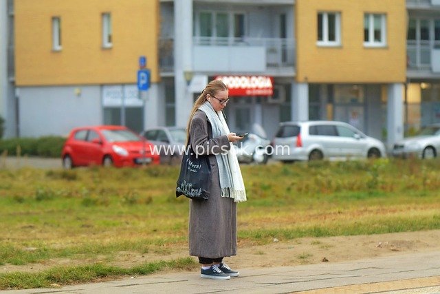 Daily Moment: Young Woman Browsing Phone in Front of Urban Residence, Casual Outfit