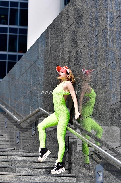 Young Woman in Neon Green Sportswear Posing Energetically on Urban Stairs