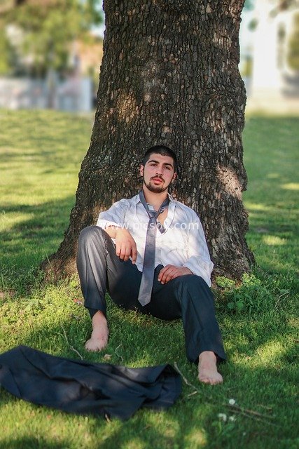 Young Man Under a Tree in Sunny Park: Emotional Portrait in White Shirt and Gray Pants