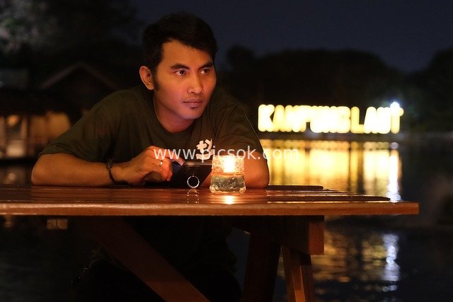 Man with Phone by Candlelight at Riverside at Night: Contemplative Waiting Scene