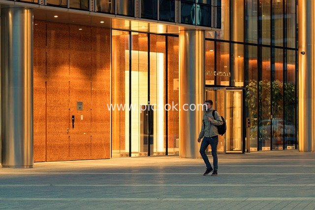 傍晚背背包青年漫步现代玻璃建筑前